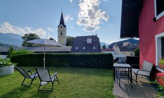 A beautiful garden with lounge chairs and a table. In the background, a church and a clear sky can be seen.