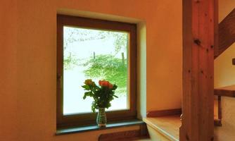 A cozy hallway with a wooden staircase and a window that looks out into the greenery. On a windowsill is a vase with flowers.