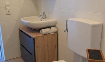 A modern bathroom with a toilet, a sink, and a mirror. The color scheme is bright and simple, with minimalist furniture.