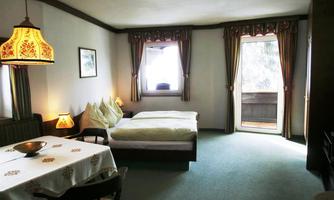 A cozy room with two single beds and a small dining area. The windows let in plenty of light and provide access to a balcony.