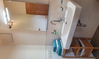 A modern bathroom with a sink, a large mirror, and a wooden shelf. Clean towels in various colors are neatly placed on the shelf.