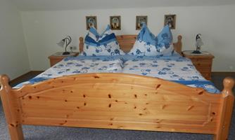 A cozy bedroom with a wood-colored bed and blue bedding. Pictures hang on the walls, and lamps are on the nightstands.