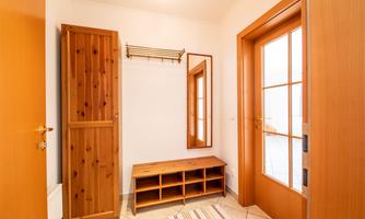 A bright entrance area with wooden cabinets and a mirror. The floor is tiled and a shoe rack can be seen.