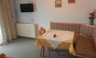 A cozy room with a dining table and a bench. Two pictures hang on the wall, and there is a television.