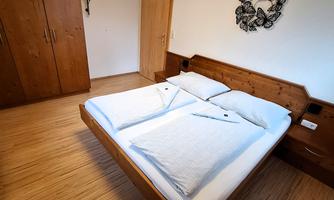 A simple bedroom with a double bed and wooden wardrobes. The walls are light and there is a decorative wall design.