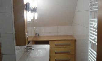 A modern bathroom with a sink and wooden cabinets. The walls are brightly tiled, and there is a towel heater.