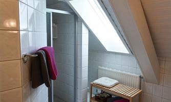 A modern bathroom with a shower. There is a wooden bench and towels in various colors.