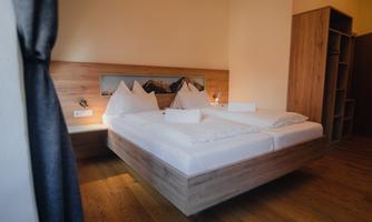 A modern bedroom with a large double bed and wooden decor. The walls are bright, and the room is well-lit.
