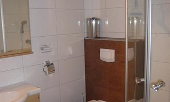 A modern bathroom with a shower, sink, and toilet. The walls are tiled in white and there are wooden elements for a warm accent.