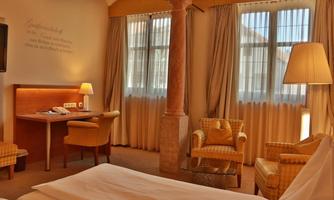A cozy hotel room with a large window, a desk area, and comfortable armchairs. The decor is designed to be modern and welcoming.