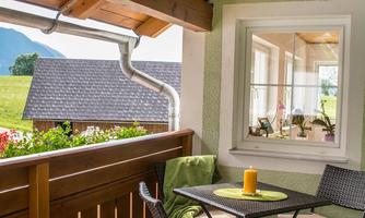 A cozy balcony with a small table and chairs. In the background, green meadows and mountains can be seen.