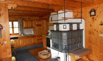 A cozy kitchen with wood ceilings and walls. At the center is a traditional oven and a kitchen unit clad in wood.