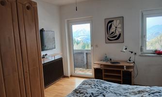 A cozy bedroom with wooden cabinets and a television. The windows offer a view of the mountains.