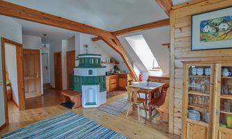 A cozy room with wooden ceilings and walls. There is a traditional stove, a dining table, and a beautiful carpet.