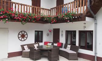 A cozy outdoor area with a round table and comfortable rattan seating. The walls are decorated with flowers and a rustic wooden railing.