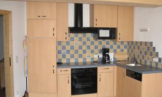 A bright kitchen with wooden cabinets and a colorful tiled wall. The amenities include a stove, a microwave, and a coffee machine.