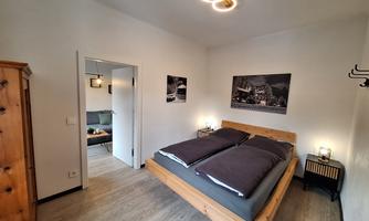 A cozy bedroom with a large wooden bed and modern decorative elements. The walls are painted light, and there are simple, stylish furnishings.