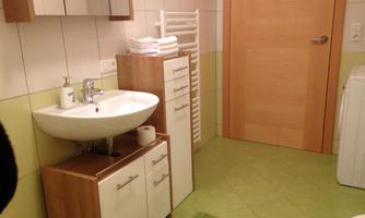 A modern bathroom with a sink and wooden cabinets. The walls are light and the floors are green.