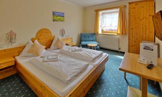 A cozy bedroom with a double bed and wooden paneling. A small table and a blue armchair complement the decor.