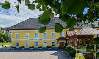 A yellow building with a landscaped entrance area and a covered outdoor space. The sky is blue with some clouds.