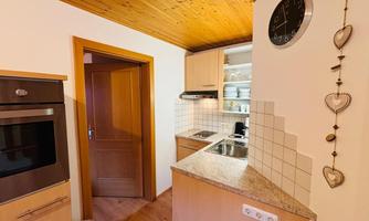 A modern kitchen with a wooden ceiling and light cabinets. The features include a stove, a sink, and a decorative wall clock.