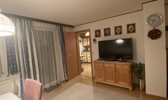 A cozy living room with a wooden cabinet and a television. Curtains and a clock complete the decor.