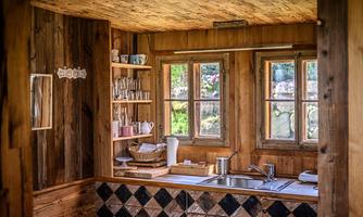 A cozy wooden kitchen with a sink and windows that let in plenty of light. Shelves with dishes and glasses give the room a warm atmosphere.