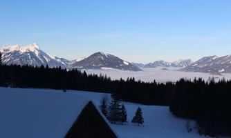 A snowy landscape with mountains in the background. The sky is clear and blue, and fog lies over the valley.