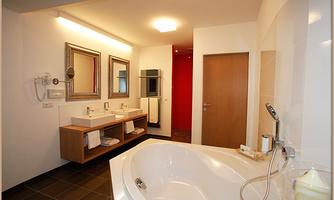 A modern bathroom with a large whirlpool and two sinks. The walls are light, with elegant mirrors and a warm atmosphere.