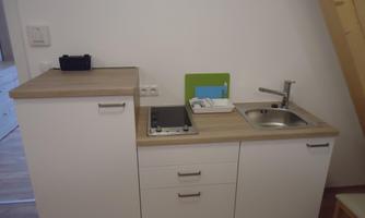 A compact kitchenette with a wooden countertop, a sink, and a cooking area. The cabinets are white and provide storage space.