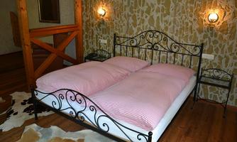 A cozy bedroom with a wrought iron bed and striped bedspreads. The walls are adorned with natural stone, and there are wooden elements and a nightstand.