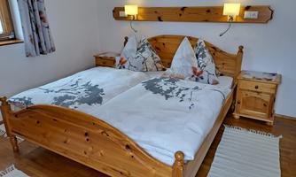 A cozy bedroom with a large double bed and wooden furniture. The walls are light, and there is soft lighting as well as decorative pillows.