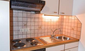 A small, modern kitchen with wooden shelves and bright cabinets. It features a stove, a sink, and an oven.
