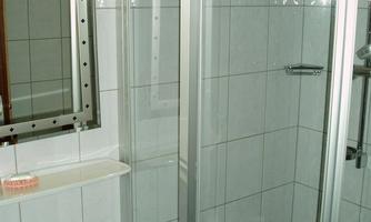A modern bathroom with a shower stall and a sink. The walls are tiled with white tiles.