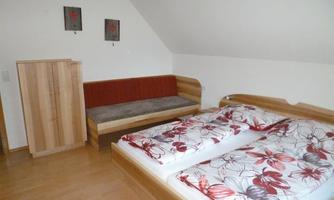 The picture shows a simple bedroom with two beds and a seating area. The walls are light, and there are decorative pictures in neutral colors.