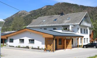A modern building with a combination of wood and plaster façade. In the background, mountains can be seen, and the sky is clear.