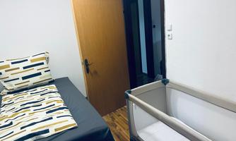 A simple bedroom with a bed and a crib. The wall is white and the door leads to another room.