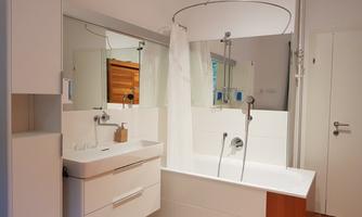 A modern bathroom with a bathtub and shower curtain. White walls and wooden details create a bright, inviting atmosphere.