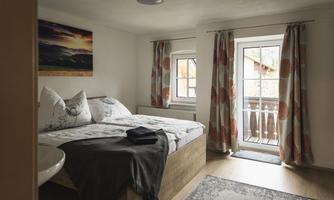 A cozy bedroom with a double bed and soft pillows. Large windows provide plenty of light and a view of the balcony.