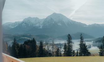 An impressive mountain landscape with snow-covered peaks and green meadows. Dense forests and misty valleys create a picturesque atmosphere.