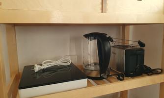 A kitchen corner with a kettle, a toaster, and a scale. The appliances are on a wooden shelf and are in good condition.