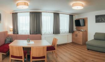 A cozy living space with a dining area and a sofa. Large windows let in plenty of daylight.