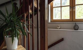 A staircase with wooden steps and a window through which daylight flows. A plant sits on a small table and gives the room a cozy ambiance.