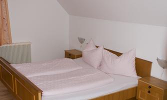 A cozy bedroom with a double bed and two nightstands. The walls are white and the floor is made of wood.