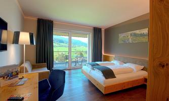 A modern hotel room with two beds and a large window. The view looks out onto a green landscape and a balcony is present.