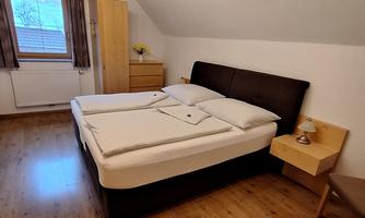 A cozy bedroom with a double bed and wooden floor. There is a wardrobe and a bedside table next to the bed.