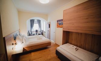 A cozy room with a double bed and a single bed. The decor is modern and bright, with large windows and a wooden floor.