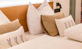 A cozy bedroom with pillows on a bed. The pillows are decorative with a lavender pattern.