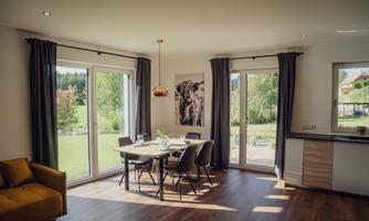 A modern living room with a dining table and chairs. Large windows let in plenty of daylight and offer a view of the outdoors.