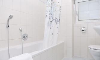 A bright bathroom with a bathtub and a shower. The walls are tiled, and there is a window for natural light.